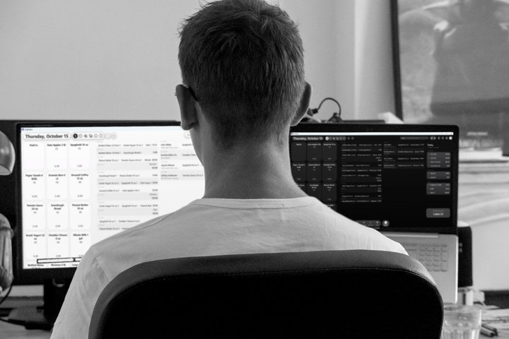 A business owner at a desk with TallyMate open on a monitor and a laptop